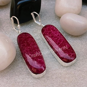 May include: A pair of silver earrings with a deep pink, oval-shaped stone. The stones have a textured surface and are set in a silver bezel.