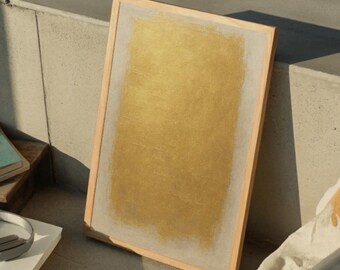 May include: A framed artwork with a gold-colored center and a light-colored border. The frame is made of light-colored wood. The artwork is leaning against a concrete surface, with other objects in the background.