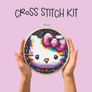 Peut inclure: Kit de point de croix avec un motif Hello Kitty coloré avec un arc-en-ciel et un nœud rose sur un fond noir avec des confettis.