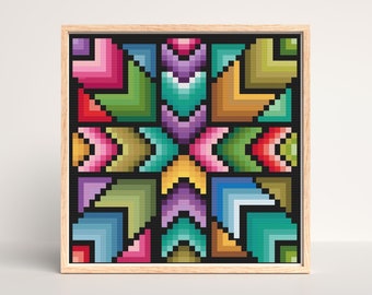 May include: A framed, square cross-stitch artwork featuring a geometric design. The design uses a variety of colors, including pink, green, purple, and yellow, arranged in a symmetrical pattern. The artwork is set in a light-colored wooden frame.