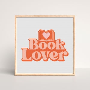 May include: Cross stitch pattern featuring the text "Book Lover" in orange and pink with a pink heart inside an open book.