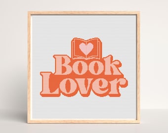 May include: Cross stitch pattern featuring the text "Book Lover" in orange and pink with a pink heart inside an open book.