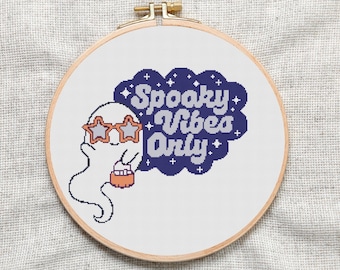 May include: A white ghost wearing star-shaped sunglasses holds a bucket of sweets in front of a blue cloud with the text "Spooky Vibes Only" in white.