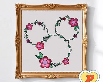 May include: Cross-stitch art in a gold ornate frame. The design features a floral Mickey Mouse head shape, with pink flowers and green leaves. The background is white. A yellow heart-shaped sticker with a letter "P" is in the bottom right corner.