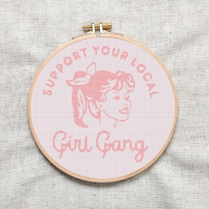 Può includere: Cerchio da ricamo rosa con il testo "Support Your Local Girl Gang" e un'illustrazione rosa di una donna con una fascia per capelli.