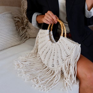 Macrame woven tote bag with fringe laying on the sofa with girl holding it wooden handles