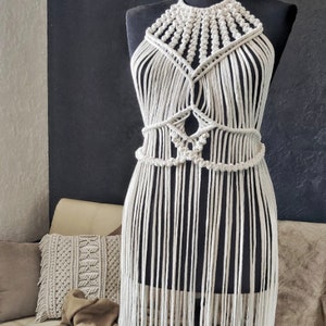 May include: A white macrame halter top with a fringe bottom. The top is made with a thick cotton cord and has a geometric pattern.