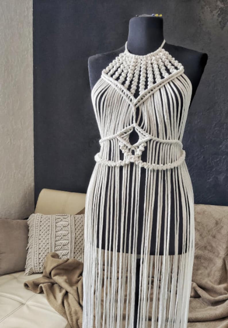May include: A white macrame halter top with a fringe bottom. The top is made with a thick cotton cord and has a geometric pattern.