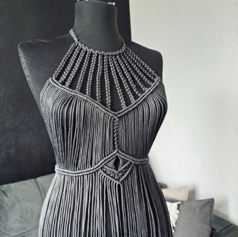 May include: A grey macrame halter top with a geometric design. The top is made of thin cords and has a fringe detail.