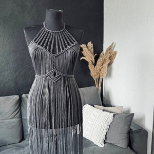 May include: A grey macrame halter top with fringe detailing. The top is displayed on a mannequin against a black background.