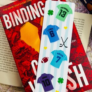 May include: A bookmark with a light blue and white striped background featuring jersey illustrations with names and numbers. A book with the title "Binding 12" is in the background.
