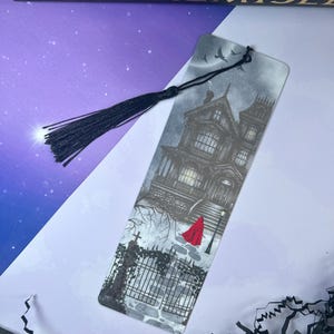 May include: A bookmark featuring a detailed illustration of a haunted house with a red-cloaked figure. The bookmark has a black tassel and the text "SenLinYu: Alchemise" at the top. The artwork is in shades of gray and black.