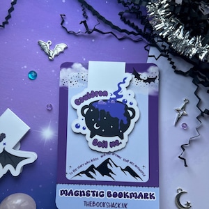 May include: A purple and white magnetic bookmark featuring a black cauldron with the text "Boil Me". The bookmark has a mountain and star design with the text "To the stars who listen and the dreams that are answered". The bookmark is from THEBOOKSHACK.UK.