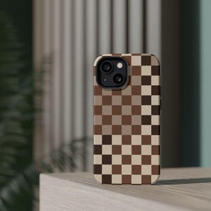 May include: A brown and beige checkered phone case with a black camera lens.