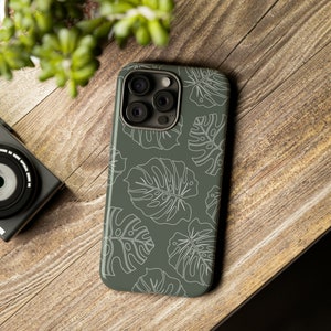 May include: A green phone case with a white outline of tropical leaves. The case has a camera lens cutout.