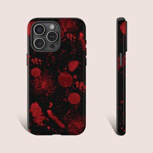 May include: A black phone case with a red splatter pattern. The case has a cutout for the camera lens.