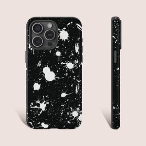 May include: Black phone case with a white splatter paint design. The case has a glossy finish and a camera cutout. The side view shows the case's thickness and button placement. The design is abstract and artistic.