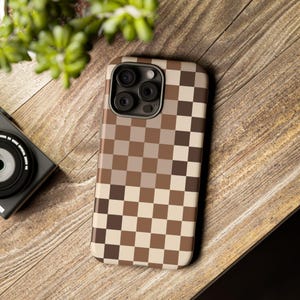 May include: A brown and beige checkered phone case with a camera lens cutout. The case is made of a durable material and is designed to protect your phone from scratches and bumps.
