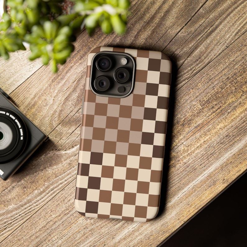 May include: A brown and beige checkered phone case with a camera lens cutout. The case is made of a durable material and is designed to protect your phone from scratches and bumps.