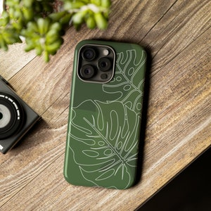 May include: A green phone case with a white outline of tropical leaves. The case has a camera lens cutout and a raised lip around the edges.