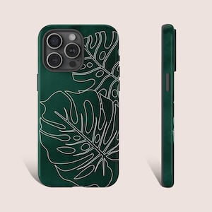 May include: A dark green phone case with a white outline of tropical leaves. The case has a cutout for the phone's camera.