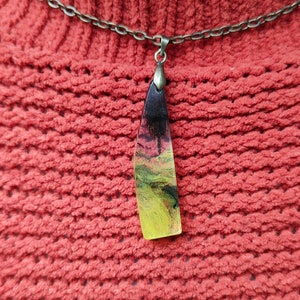 May include: A necklace with a long, thin, yellow, black, and brown resin pendant. The pendant is shaped like a teardrop and has a swirl pattern.