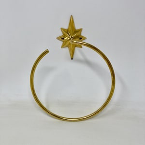 May include: A gold-colored towel ring with a starburst design. The ring is circular and attached to a star-shaped mount with a pointed center. The star has eight points and small black accents. The design is likely for a bathroom.