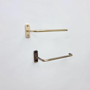 May include: Two wall-mounted towel racks. The top rack is a light gold color, and the bottom rack is a darker, antique gold color. Each rack has a rectangular mounting plate with two screws.