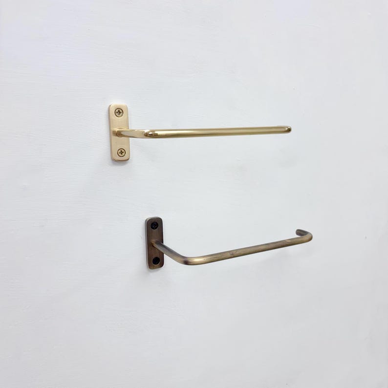 May include: Two wall-mounted towel racks. The top rack is a light gold color, and the bottom rack is a darker, antique gold color. Each rack has a rectangular mounting plate with two screws.