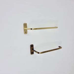 May include: Two metal towel racks. The top rack is gold-colored, and the bottom rack is a darker, bronze color. Both racks are mounted on a white wall. The top rack is a straight bar, while the bottom rack has a curved design.