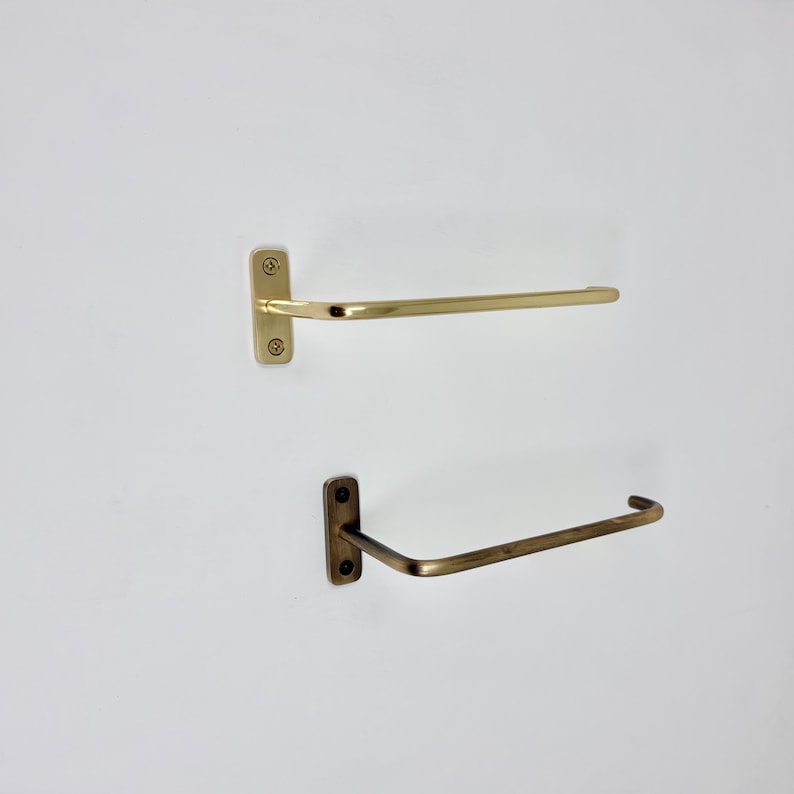 May include: Two metal towel racks. The top rack is gold-colored, and the bottom rack is a darker, bronze color. Both racks are mounted on a white wall. The top rack is a straight bar, while the bottom rack has a curved design.