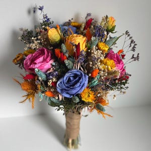 May include: A vibrant bouquet of dried flowers featuring a variety of colors. The arrangement includes pink, yellow, and blue roses, along with orange and yellow accents. The stems are wrapped in twine.