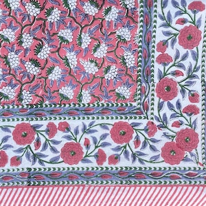Peut inclure: Une nappe en coton rose et blanche avec un imprimé floral. La nappe a une bordure avec un motif floral bleu et vert. La nappe a une bordure rayée rose et blanche.