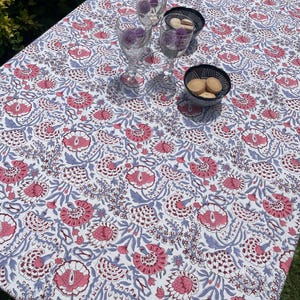 Peut inclure: Une nappe rectangulaire blanche avec un motif floral dans les tons de rose et de bleu. La table est dressée avec trois verres à vin transparents et deux petits bols contenant des biscuits. La nappe mesure environ 183 cm de long et 122 cm de large.
