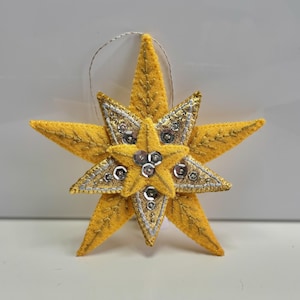 May include: A yellow felt star ornament with gold and silver sequins. The star has a loop for hanging.