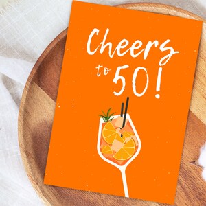 May include: Orange card with the text "Cheers to 50!" in white. A white glass with an orange drink and a sprig of rosemary is illustrated on the card.