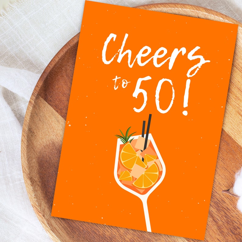 May include: Orange card with the text "Cheers to 50!" in white. A white glass with an orange drink and a sprig of rosemary is illustrated on the card.
