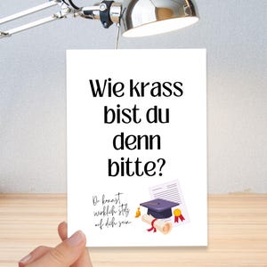 Könnte beinhalten: Eine weiße Grußkarte mit schwarzem Text, der lautet: "Wie krass bist du denn bitte?" und "Du kannst wirklich stolz auf dich sein." Eine Abschlusskappe, ein Diplom und eine goldene Medaille sind unten abgebildet.