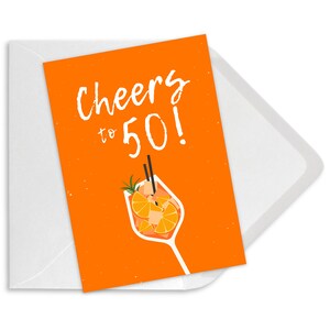 May include: Orange card with the text "Cheers to 50!" in white. An illustration of a glass of orange juice with a straw and orange slices is below the text.