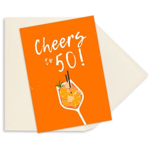May include: Orange birthday card with the text "Cheers to 50!" in white. The card features a cartoon illustration of a glass of orange juice with a sprig of rosemary and orange slices.