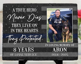 May include: A memorial plaque with a photo of a police officer and a dog. The plaque has the text "A True Hero Never Dies They Live On In The Hearts They Protected." It also says "In Loving Memory of Aron 2014-2025."