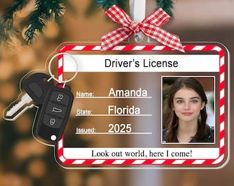 May include: A clear, customized Christmas ornament shaped like a driver's license, featuring a photo, the name "Amanda," and "Florida" as the state. The ornament includes car keys and a red and white checkered bow. Text reads "Look out world, here I come!"