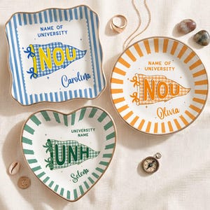 May include: Three decorative ceramic dishes in different shapes: square, round, and heart-shaped. Each dish features a university pennant design with a name and text. The square dish has blue stripes, the round dish has orange stripes, and the heart-shaped dish has green stripes.