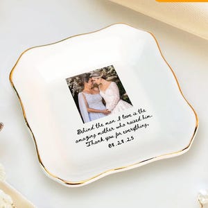 May include: White ceramic trinket dish with a gold rim and a photo of two women. The dish has the text "Behind the man I love is the amazing mother who raised him. Thank you for everything, 08.28.25."