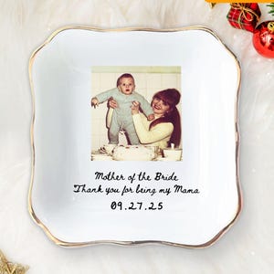 May include: A white ceramic dish with a gold rim, featuring a vintage photograph of a mother and child. The text "Mother of the Bride" and a personal message are printed on the dish. The dish is square with wavy edges.