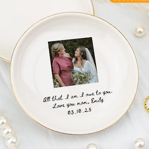 May include: A white ceramic mug with a black handle and the text "But First, Coffee" in a handwritten style. The mug is on a white surface. The mug is approximately 4 inches tall.