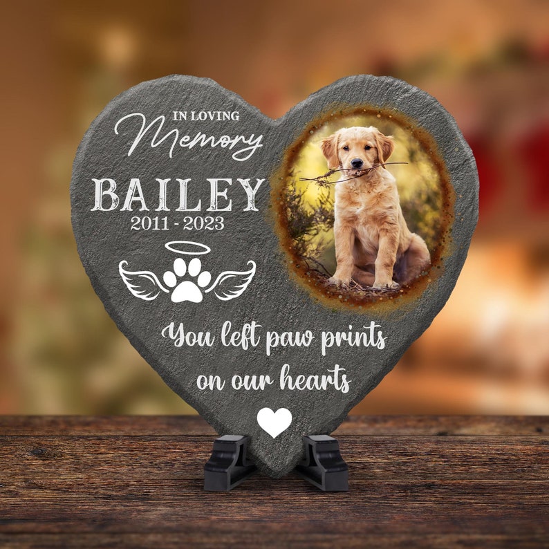 Pu&ograve; includere: Un memoriale in ardesia grigia a forma di cuore con una foto di un cucciolo di golden retriever. L'ardesia ha il testo "In loving memory Bailey 2011-2023" e "You left paw prints on our hearts".