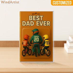 May include: A customized figurine set on a brown background, featuring a father and two children on bicycles. The text "BEST DAD EVER" is displayed above the figures. The father figure wears a green jersey with the number 20, while the children wear orange and yellow helmets.