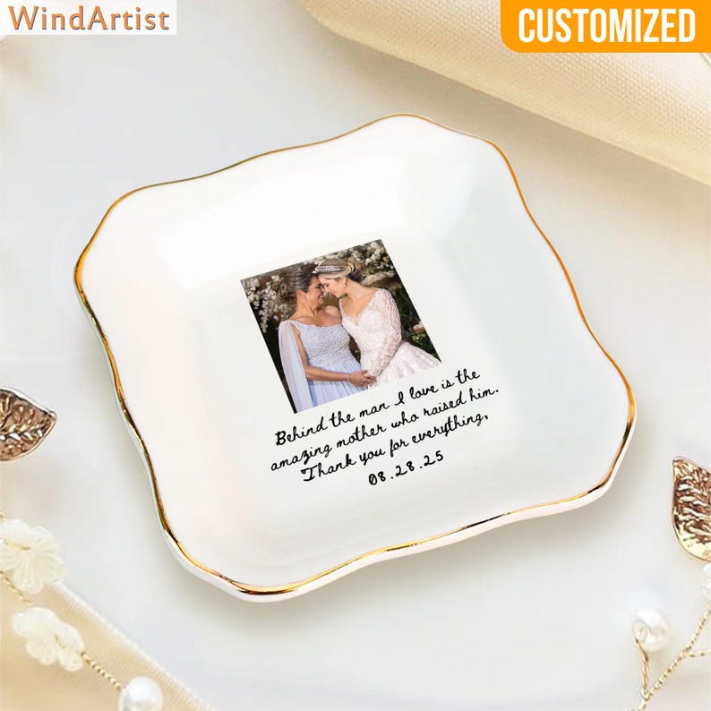 May include: White ceramic trinket dish with a gold rim and a photo of two women. The dish has the text "Behind the man I love is the amazing mother who raised him. Thank you for everything, 08.28.25."