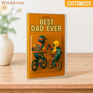 May include: A customized gift featuring two figures on bicycles, with the text "BEST DAD EVER." The figures wear helmets and jerseys with the names "DADDY" and "DAVID" and the numbers "20" and "01." The background is orange.